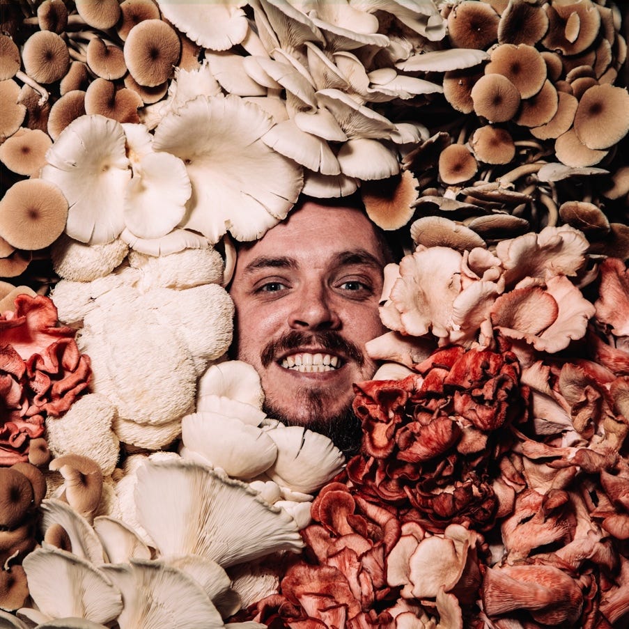 A person smiling in a pile of mushrooms

Description automatically generated