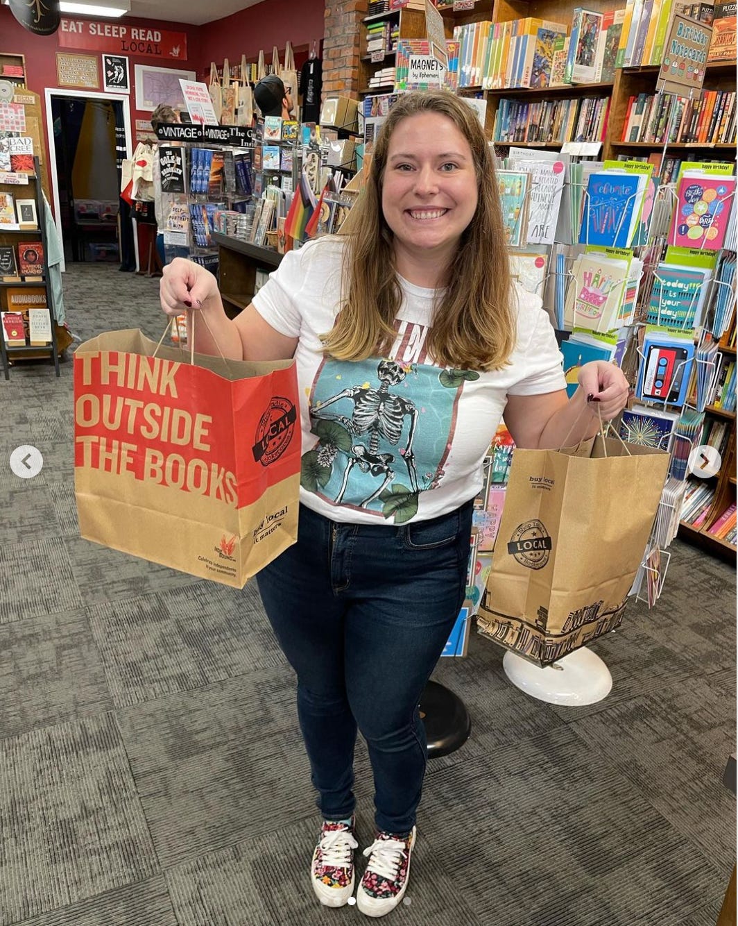 Me, a 30-something white woman, in a small bookstore holding up two bags full of books. 