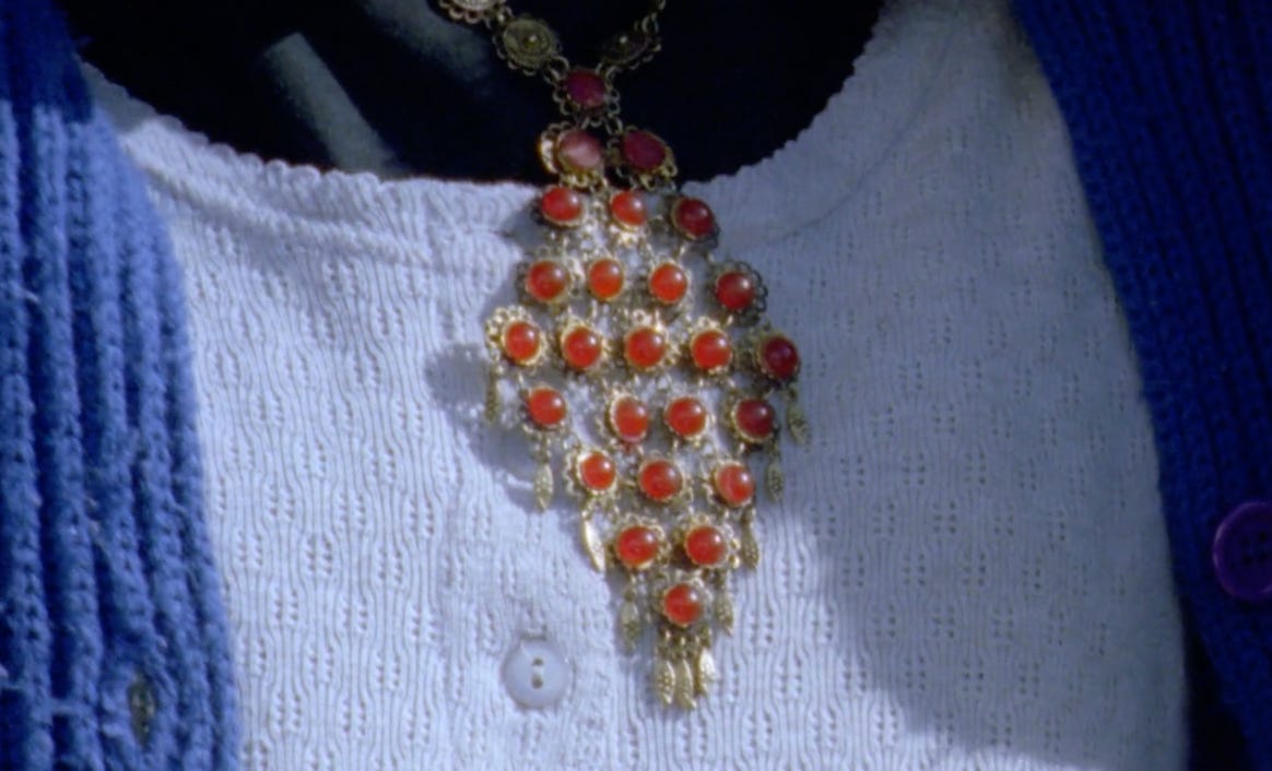 a necklace with 25 red jewels arranged in a diamond shape laying against a blue shirt