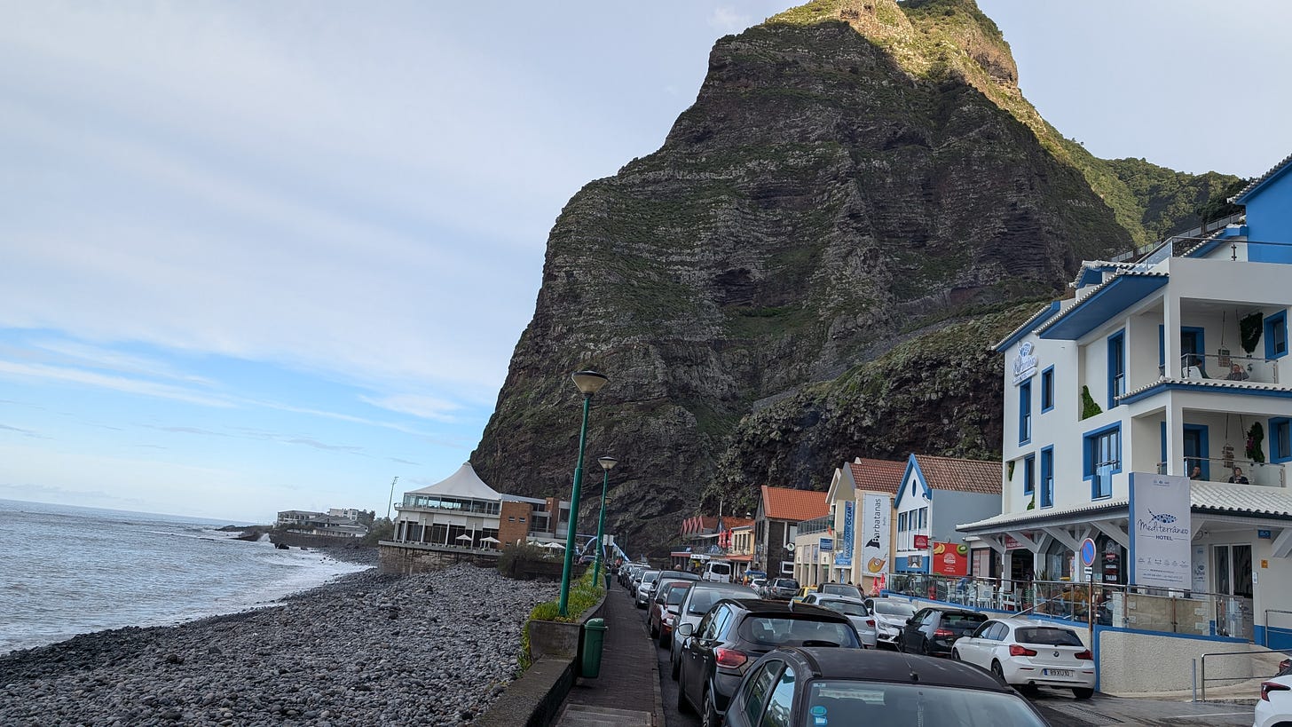 A view from the side of the little town I'm staying in. A huge cliff face is before us, against the sea on the left. A small little village of buildings and life is smack against the imposing rocks. 