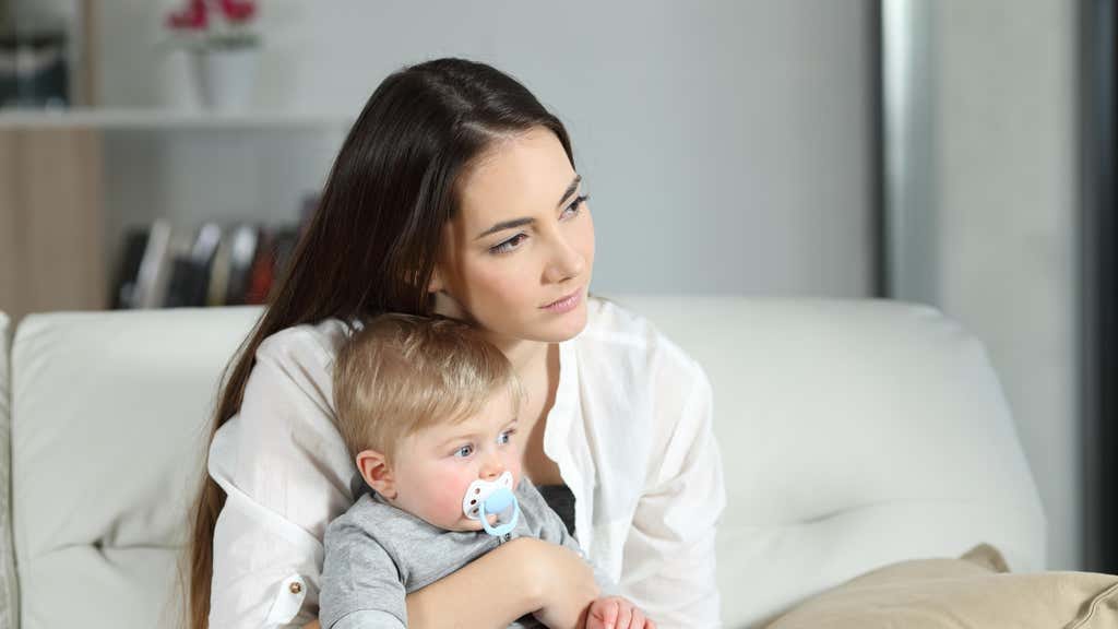 Woman looking away with her baby sitting on a couch in the living room at home