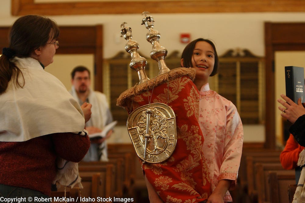 IDAHO. Boise. Asian Jewish girl carrying Torah for Hakifah in Ahavath Beth  Israel synagogue while woman touches it with Tzitzit. MR | Idaho Stock  Images