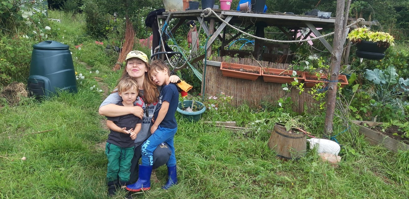 Ellese on her allotment, hugging her two young boys close to her, and wearing a yellow cap.