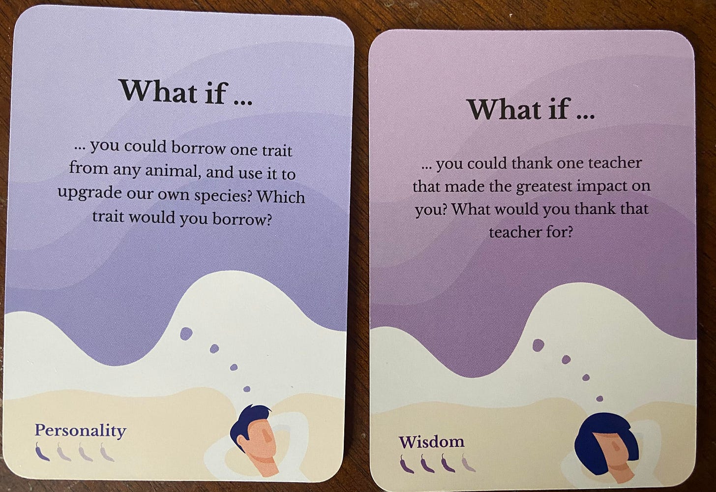 Photo of 2 cards drawn from the Scenario Cards deck. Left card says: "What if you could borrow one trait from any animal, and use it to upgrade our own species? Which trait would you borrow?" Right card says: "What if you could thank one teacher that made the greatest impact on you? What would you thank that teacher for?" 
