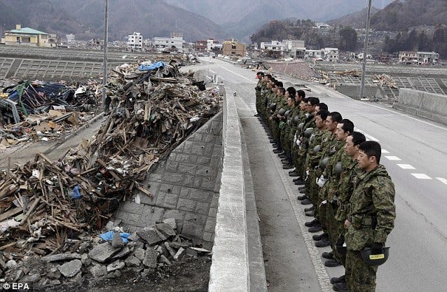 Soldados japoneses observam a destruição provocada pelo tsunami na parte exterior do muro