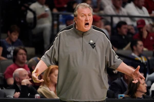 West Virginia Coach Bob Huggins stands with his hands out at his side, yelling at players during a game.