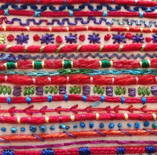 close-up of an embroidery of rows of red yarn couched with various colors of floss