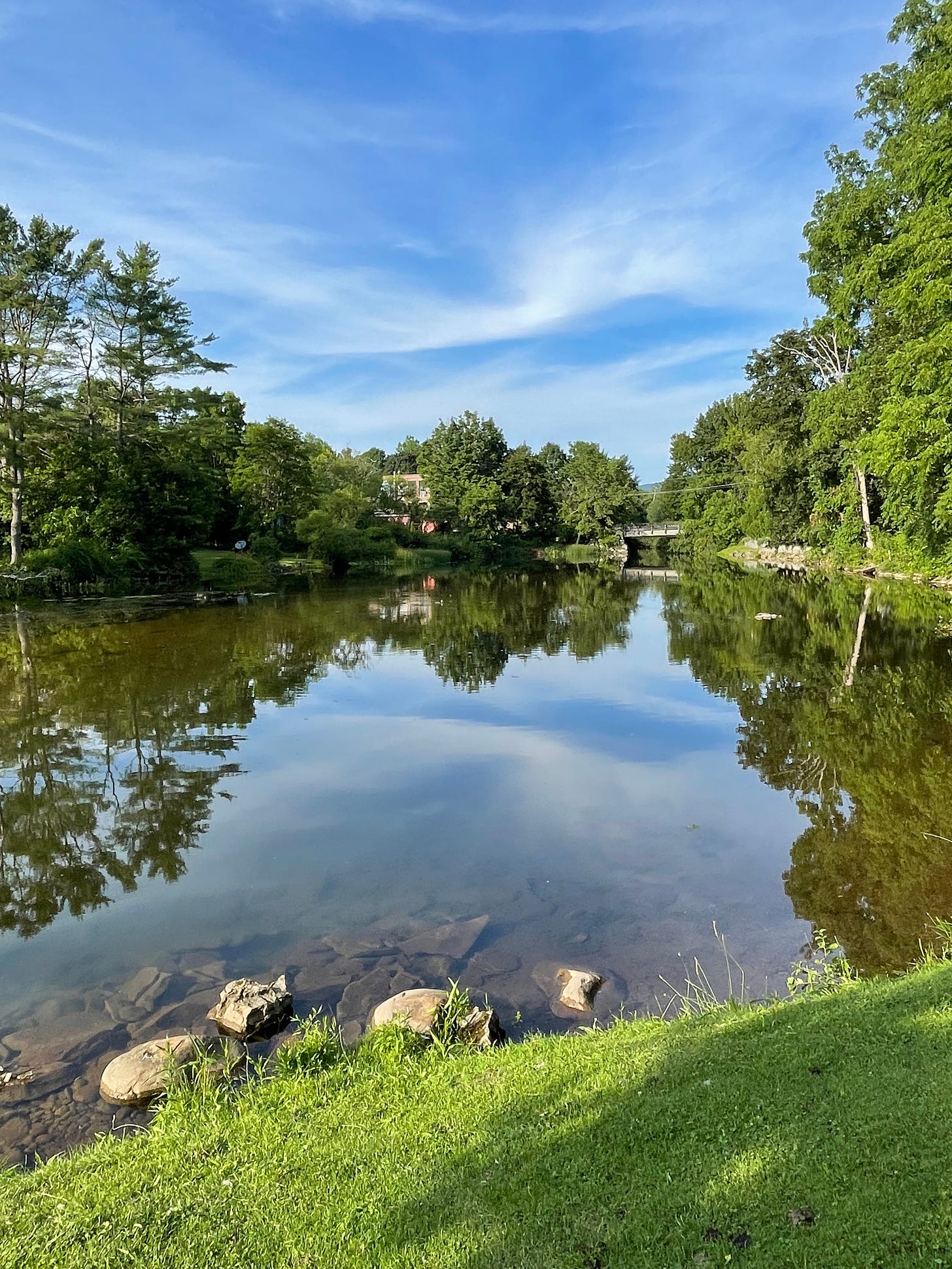 Bennington, Vermont a pond showing a reflection of the surrounding green trees and a clear blue sky. 