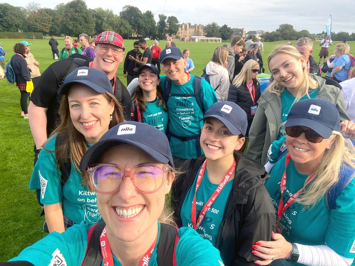 A group of smiling Nilers wearing Nile caps and t-shirts, standing in a park and getting ready to go on a long walk.