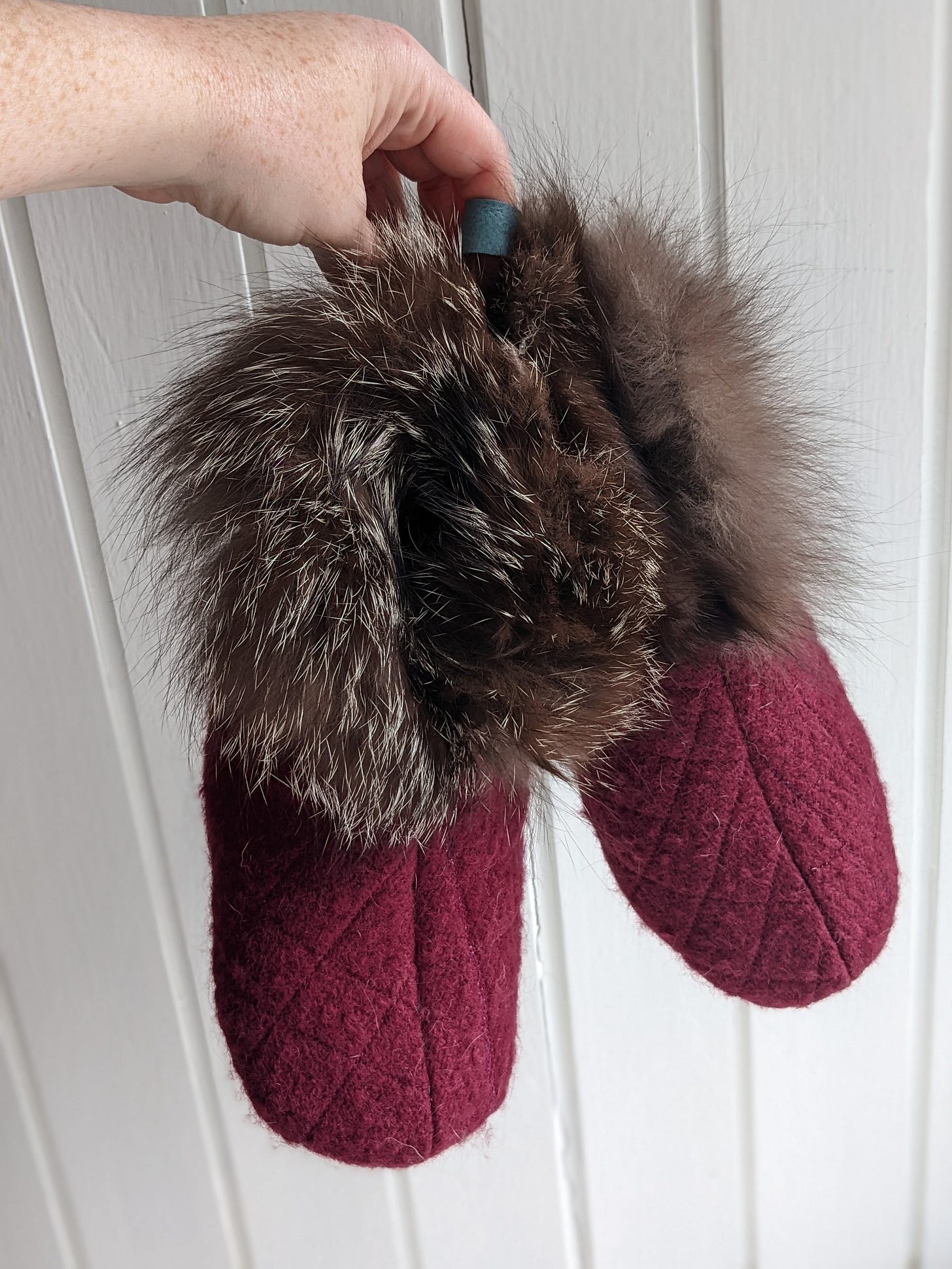A pair of burgundy wool quilted slippers with a fur cuff