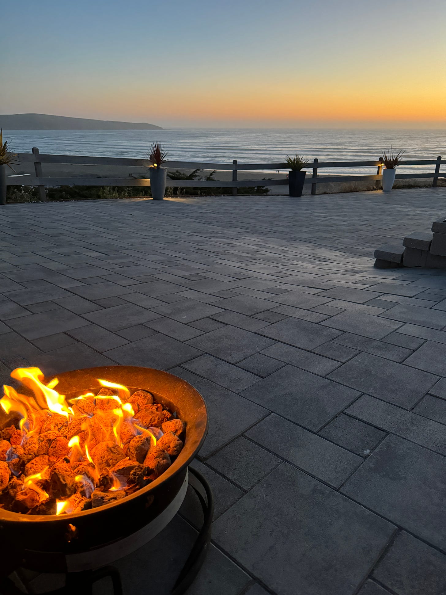 An image of a fire pit, an expanse of deck, and the sun setting over the ocean in northern California