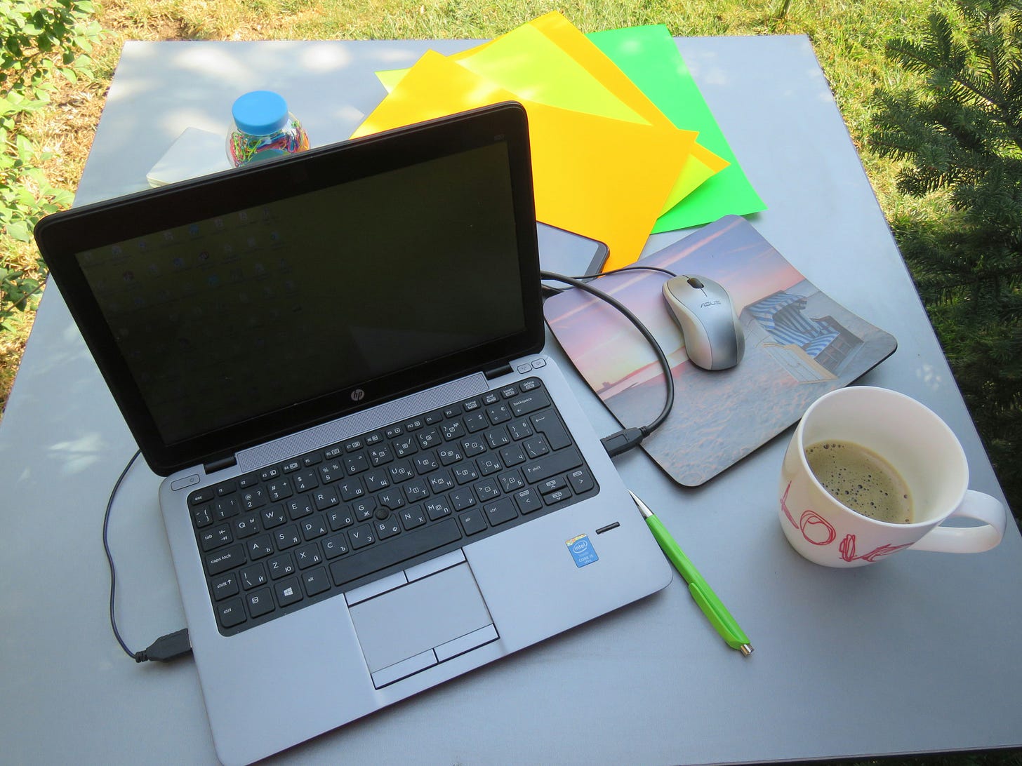 outdoors, a laptop, pen, paper, and coffee mug