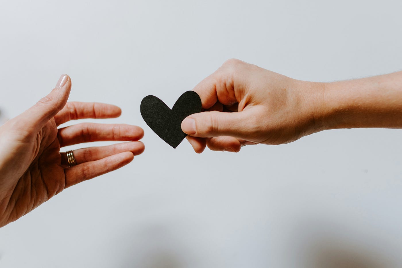 One hand offering a paper heart to another hand to show the transfer of value, personal stories and “YOU factor” to make deep connections with readers.