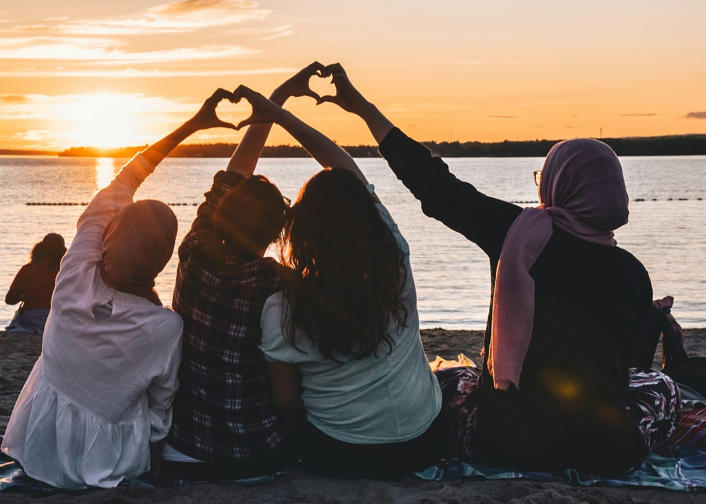 a group of multcultural friends making heart symbols with their hands, facing a sunrise