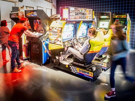 A group of people playing different arcade games in the Game On exhibition.