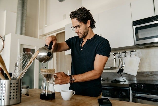man preparing pour over coffee in a white and brown kitchen