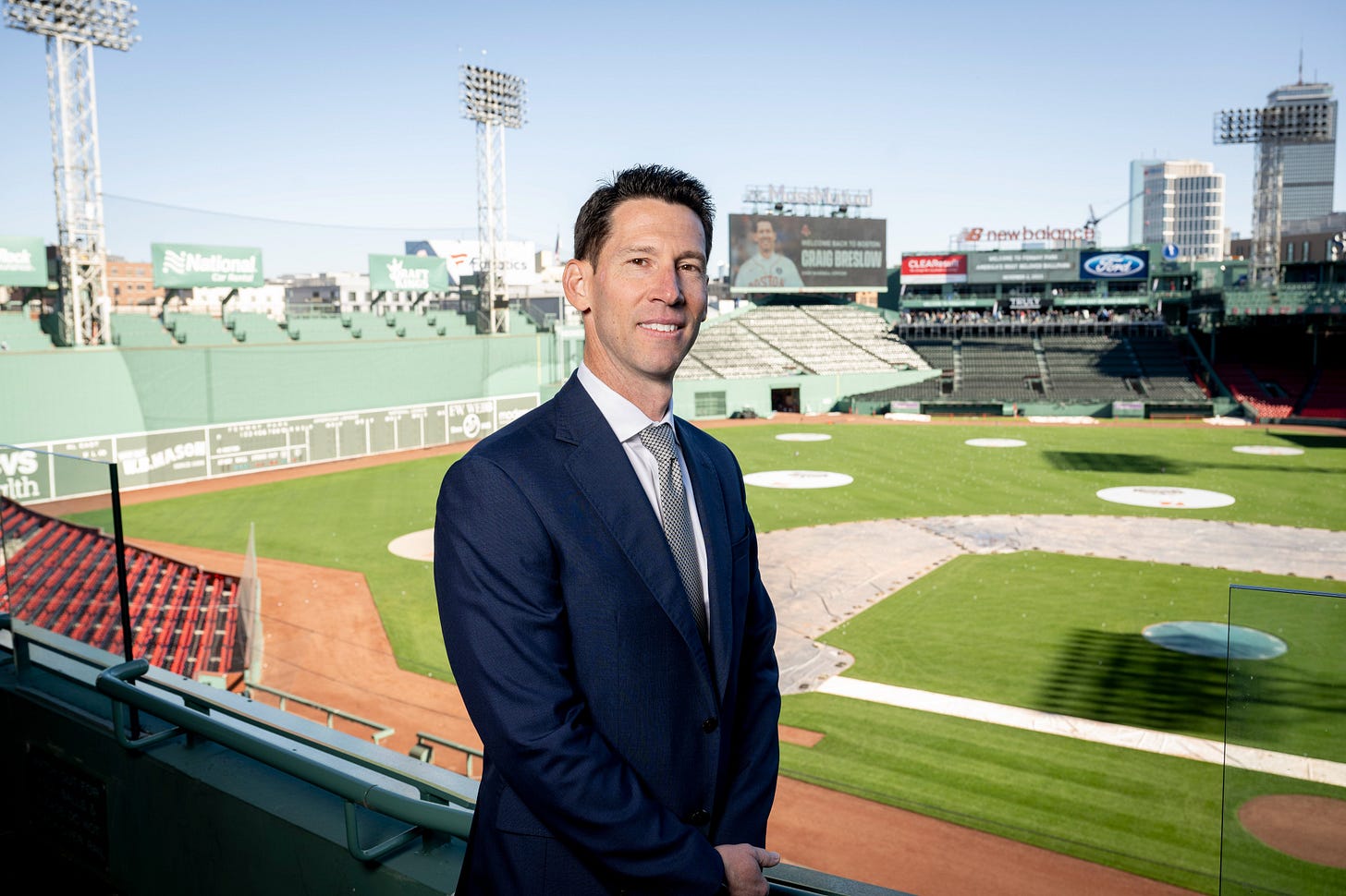 Craig Breslow poses for a picture in the stands at Fenway Park, with the field and the Green Monster behind him.
