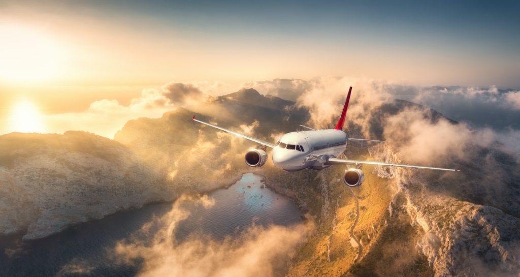 Airplane flying above mountains and low clouds at sunset