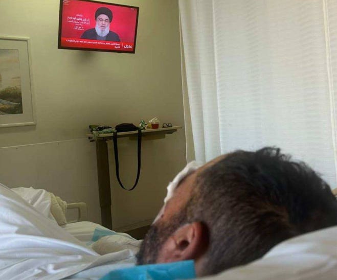 A wounded Hezbollah member watches his leader speak from hospital bed. 