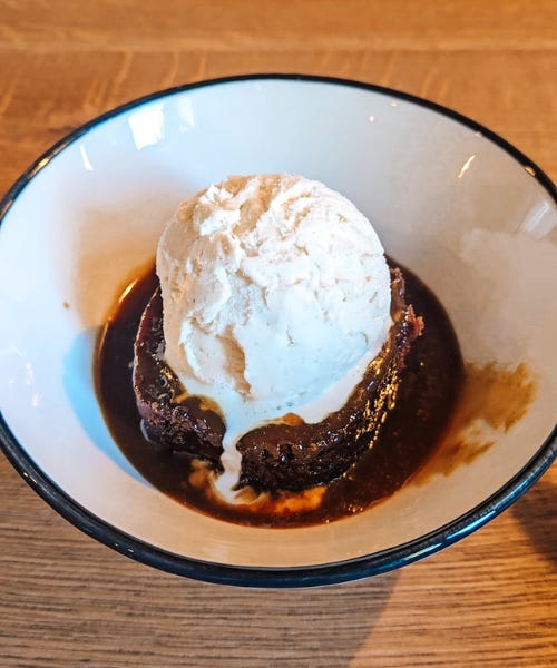 A white bowl with sticky toffee pudding and vanilla ice cream in it