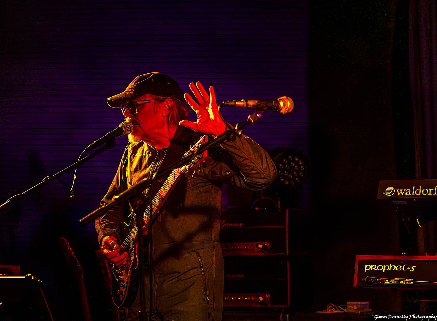 Man on stage wearing a cap and playing a guitar