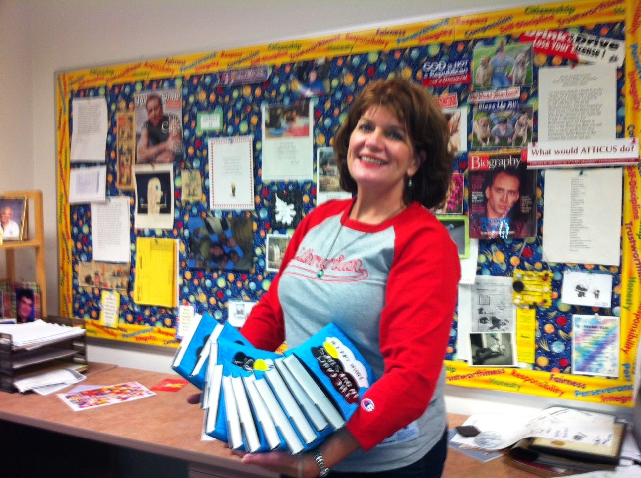 Victoria Waddle in her office holding multiple copies of The Fault in Our Stars by John Green. 