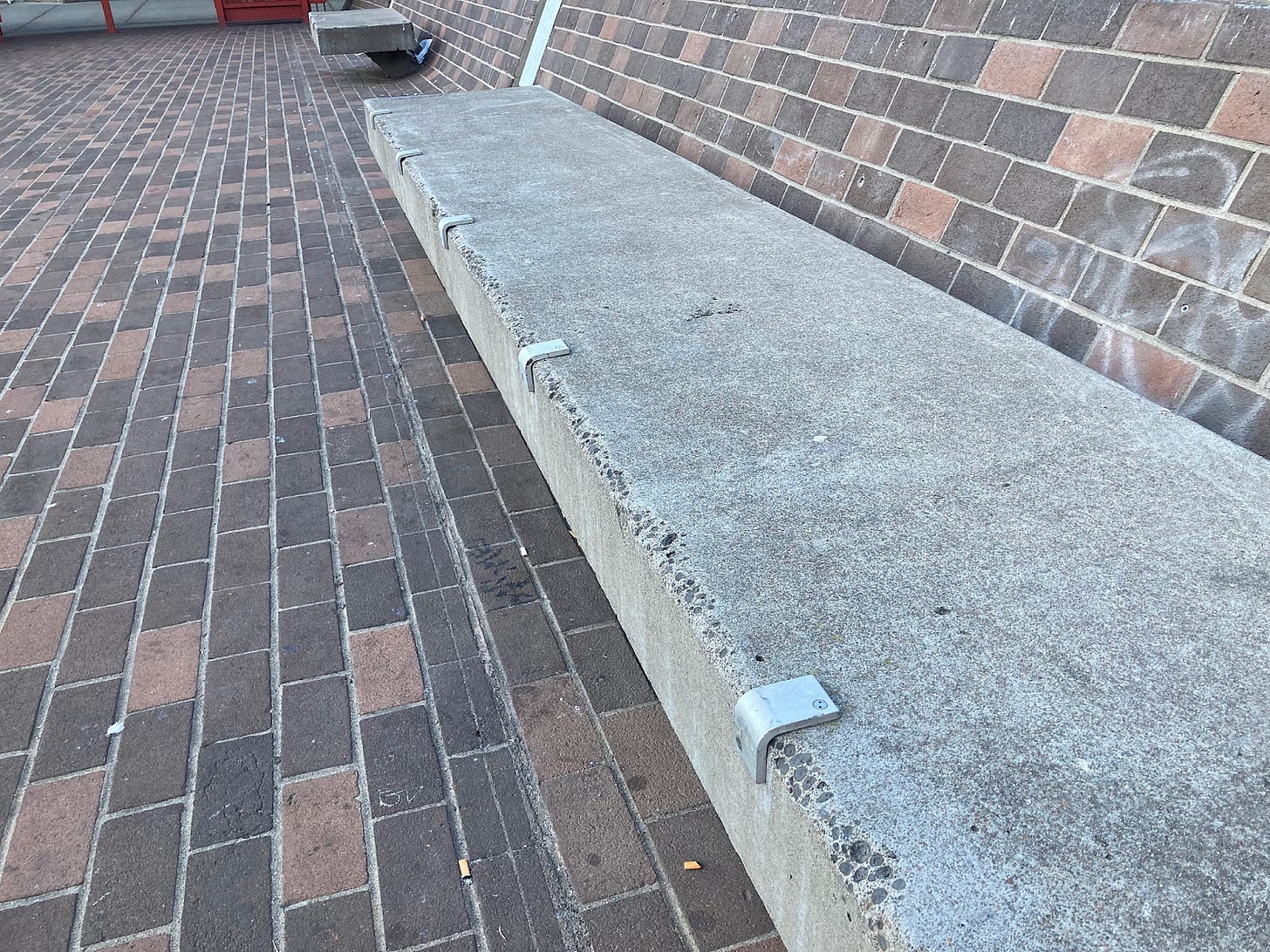 A bench that has evenly spaced corner brackets preventing skateboarders from grinding their boards along it.