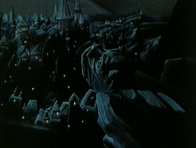 A dark image from the vantage point of a gargoyle looking over a German Expressionist-style city representing Prague.