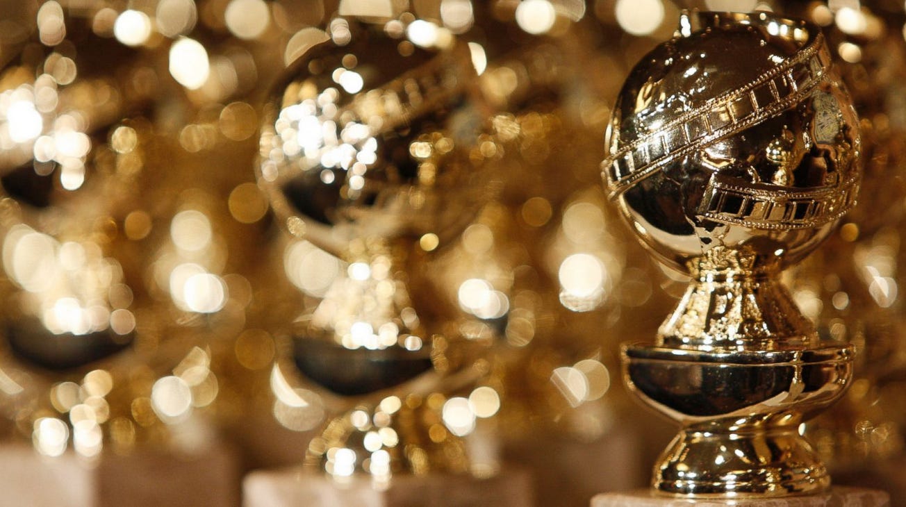 One golden globe award trophy in sharp focus in the foreground, with many blurred golden globe trophies in the background behind it