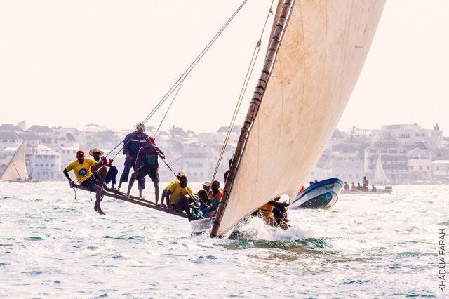 A traditional dhow loaded with about a dozen Kenyan men tilts on a bright day on the water