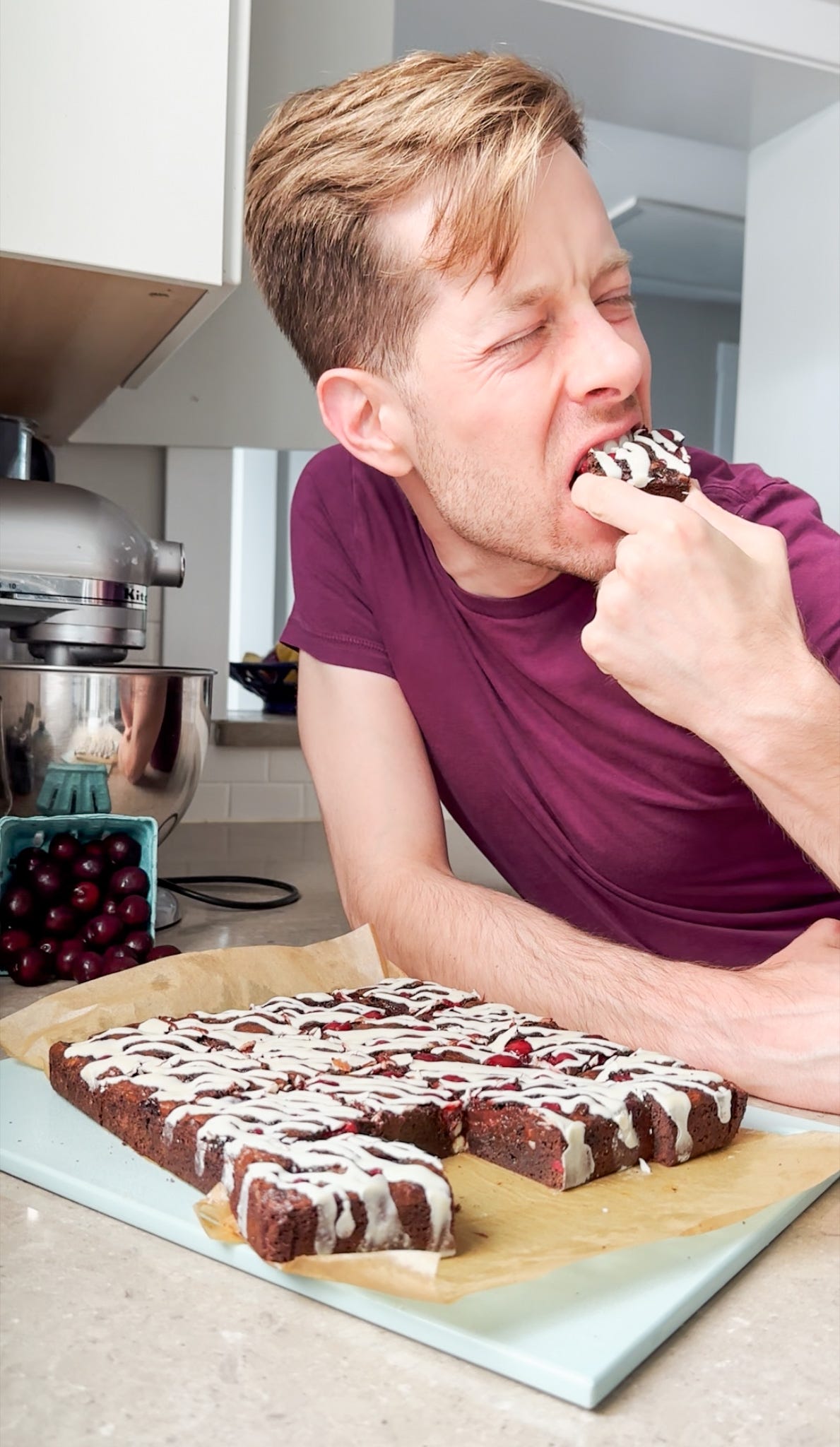 Martin biting into a brownie with a container of cherries in the background.