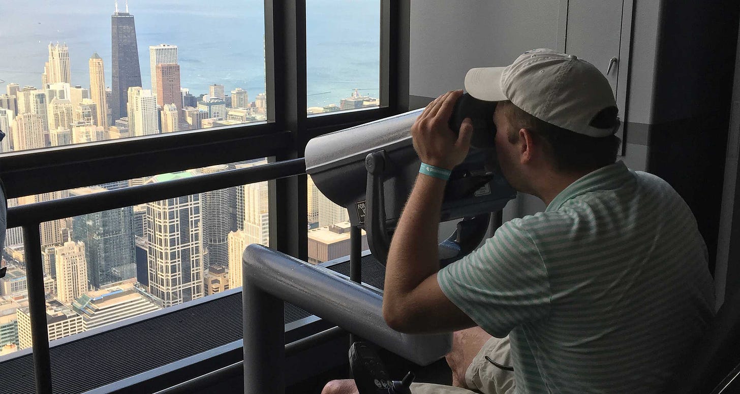 John seated in his wheelchair looking through binoculars at the Chicago skyline.