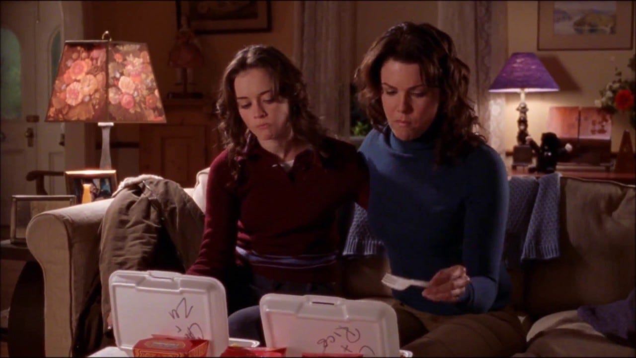 Rory and Lorelai are eating out of takeout containers in their living room. 