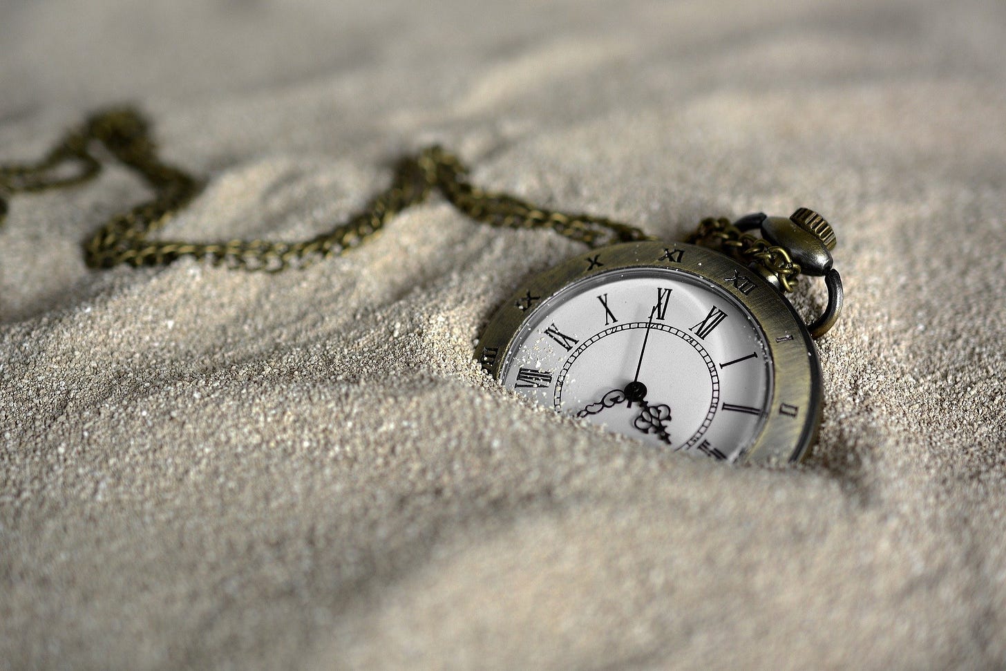 Pocket watch with Roman numerals and a chain half buried in sand
