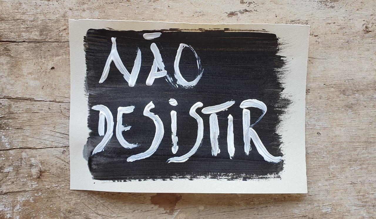Fotografia de um papel pintado de preto sobre um fundo de madeira com o escrito "Não desistir"