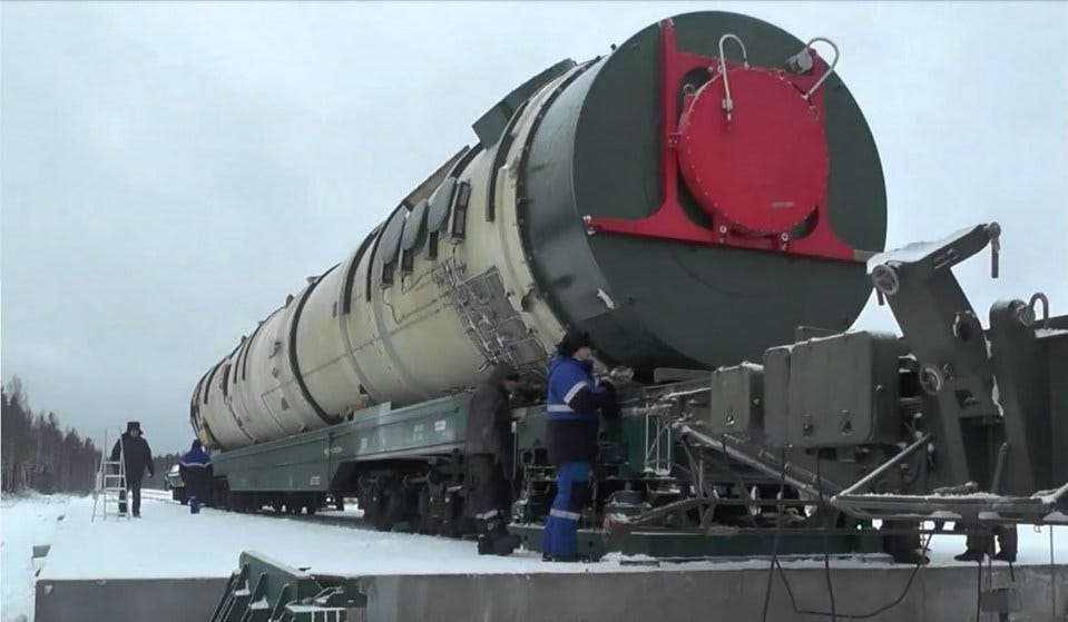 a man in a blue jacket stands next to a train with a large tank on it