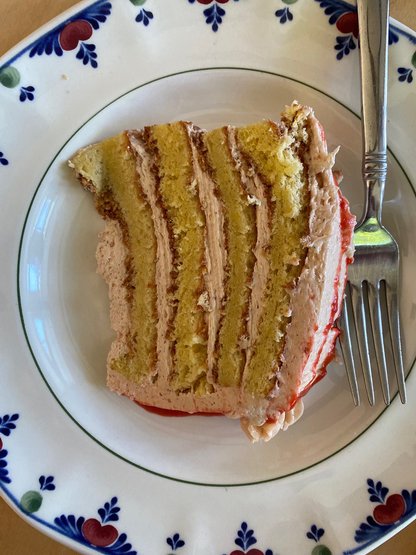 A slice of four-layer lemon cake with pink raspberry icing on a ceramic plate.