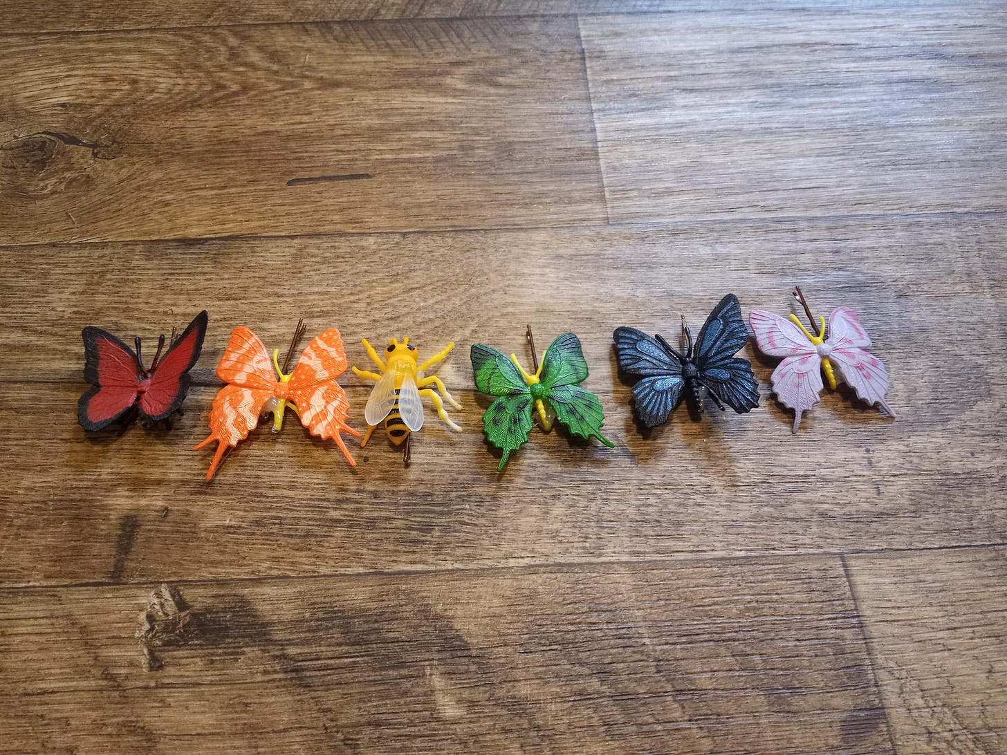 A rainbow of plastic butterfly hair clips lined up, with yellow being a bumble bee