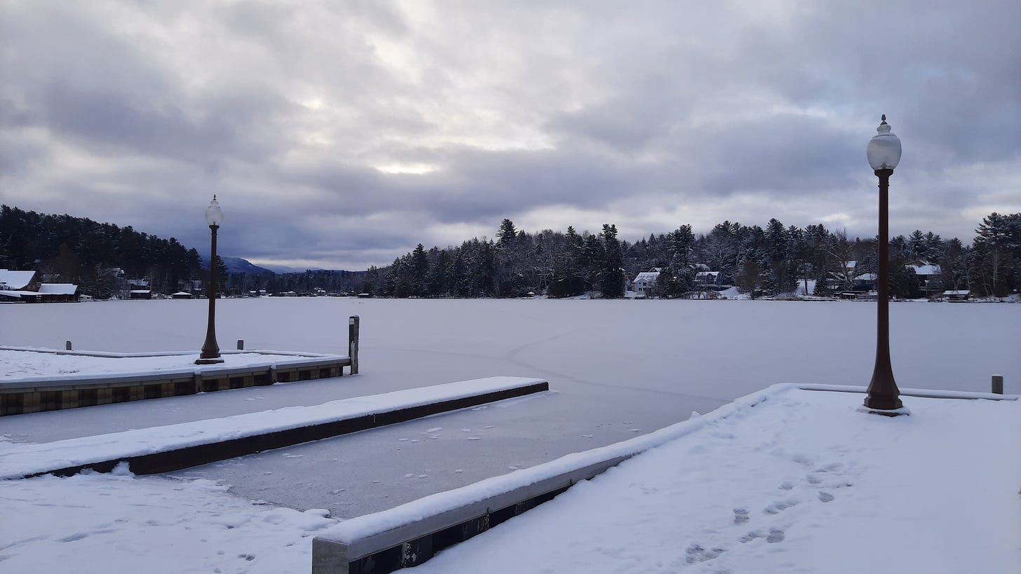 The Lake Flower boat launch is seen covered in snow, with a very thin layer of ice on the water