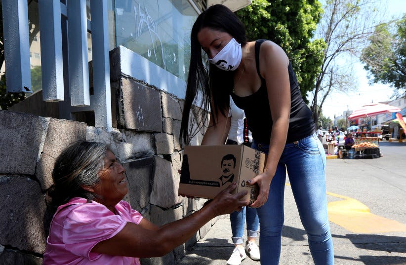 An employee of the clothing brand "El Chapo 701," owned by Alejandrina Gisselle Guzman, daughter of the convicted drug kingpin Joaquin "El Chapo" Guzman, hands out a box with food, face masks and hand sanitizers to an elderly woman as part of a campaign to help cash-strapped elderly people during th (photo credit: REUTERS)