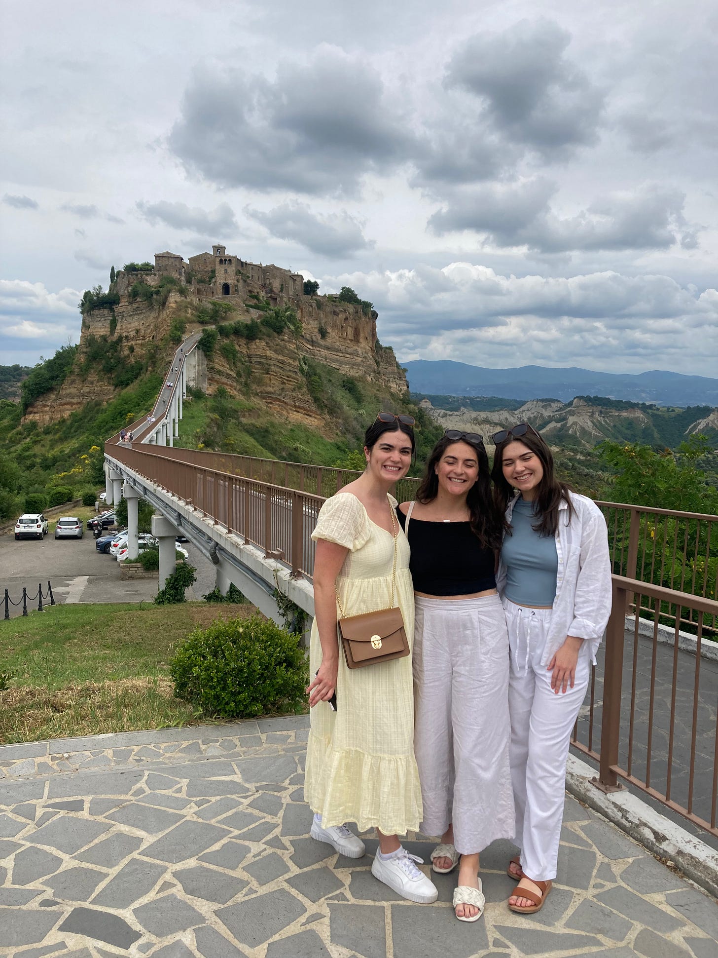 Three 20-something women posed with a hilltown in the background