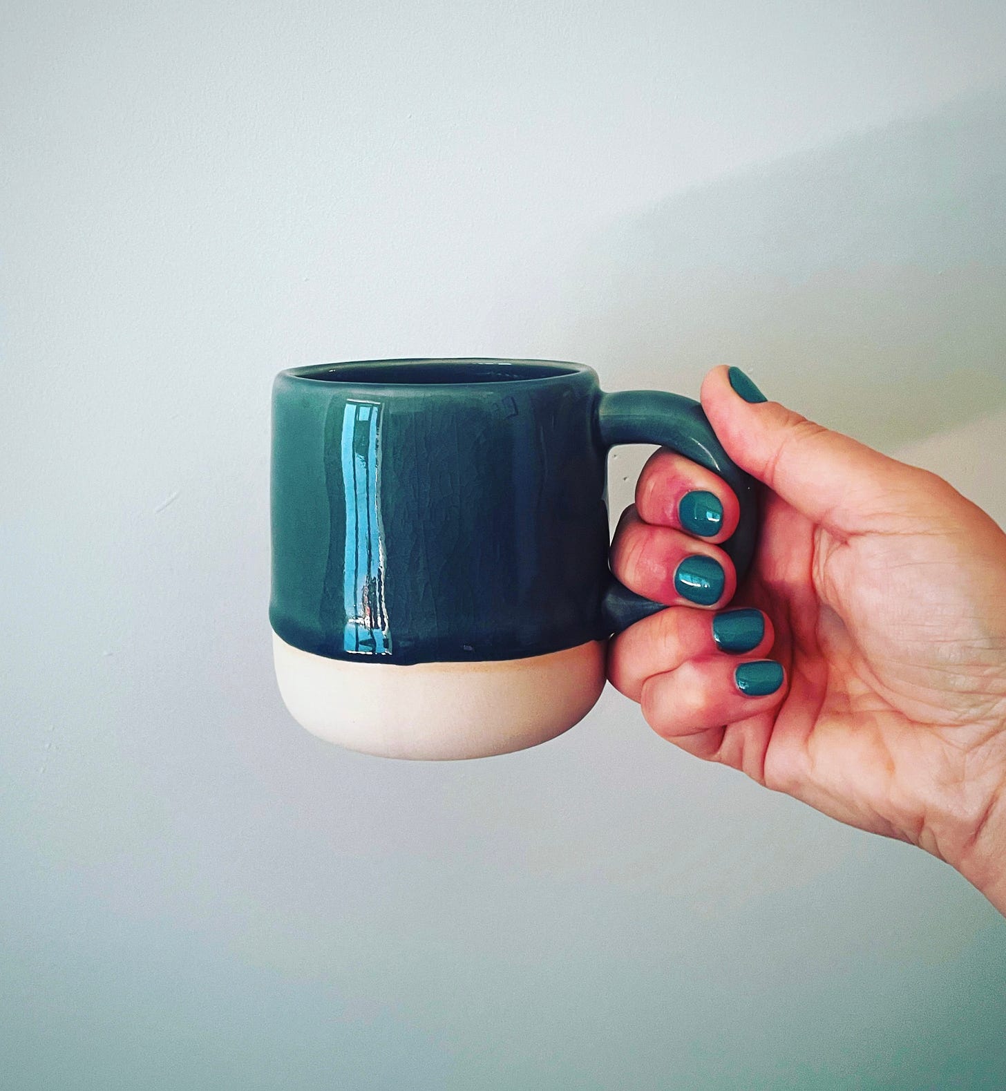 Close up of a woman's hand with teal nail polish holding a matching teal-coloured mug