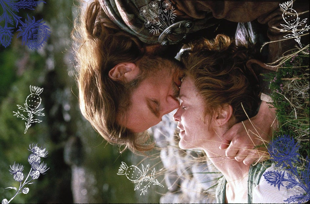 Rob Roy, played by Liam Neeson, kisses his wife Mary, played by Jessica Lange, on the forehead. Mary is lying down on grass and there is a river or loch in the background. Mary closes her eyes as Rob kisses her. Rob is wearing tartan over his brown shirt, kept in by a round sliver pin at his shoulder. Mary is wearing a white shirt and a tartan dress.
