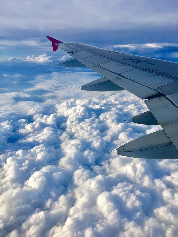 This may contain: the wing of an airplane flying over clouds