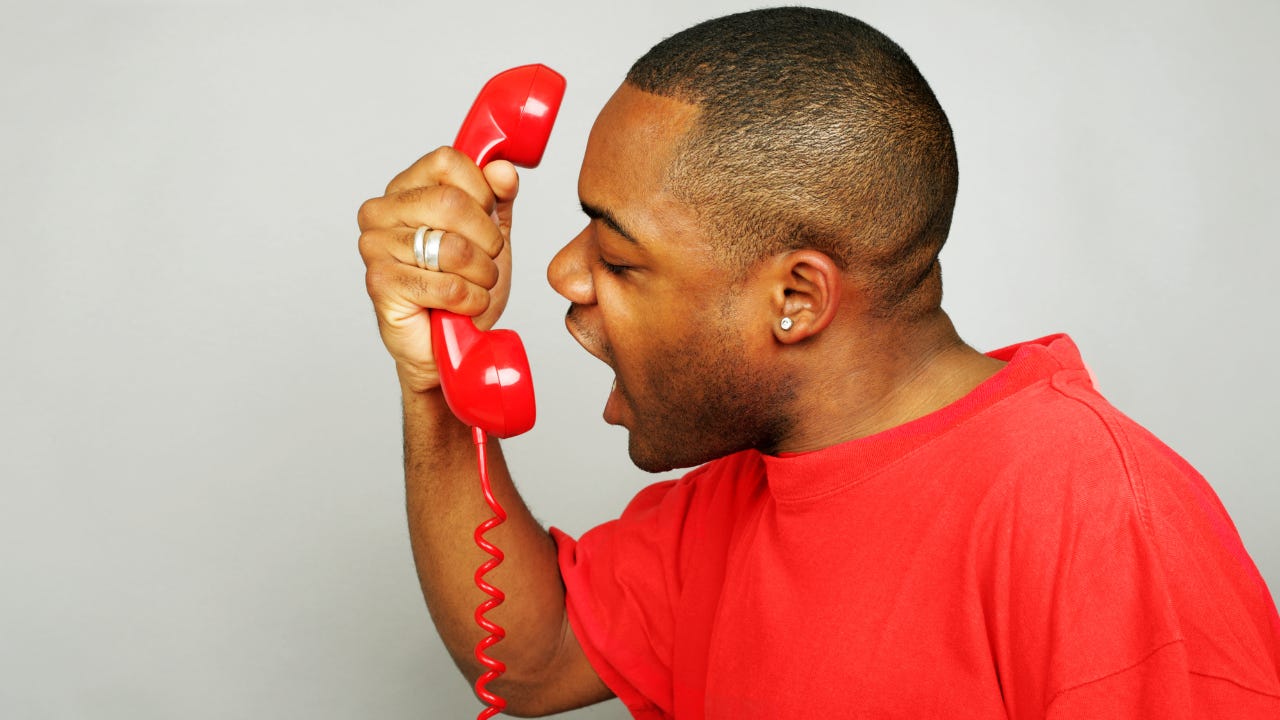 A man wearing a red shirt yelling into a red phone.
