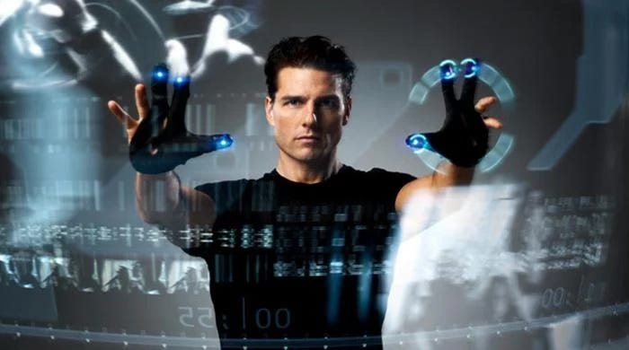 In a still from the 2002 film Minority Report, Tom Cruise manipulates objects on a huge touchscreen by means of a pair of black gloves with glowing blue lights on the fingertips.