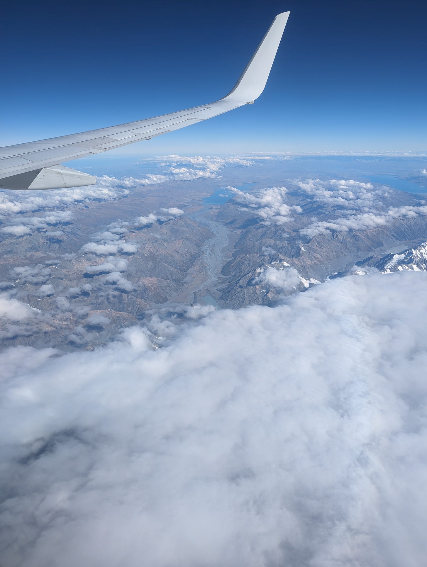 A shot from an airplane seat of the mountainous and cloud-covered terrain of New Zealand.