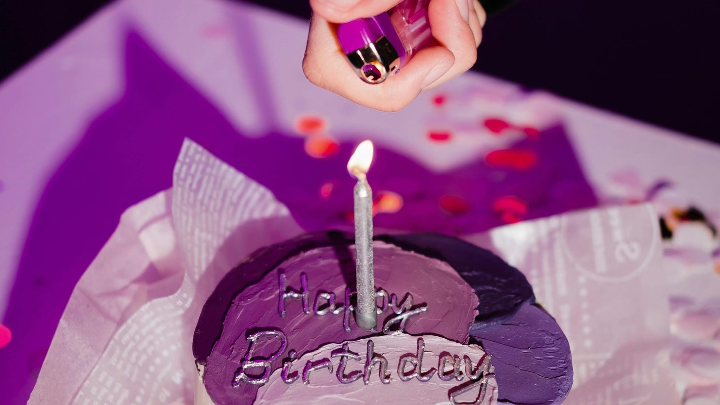 A close-up shot of a purple birthday cake and a hand using a purple Bic lighter to light a silver birthday candle.