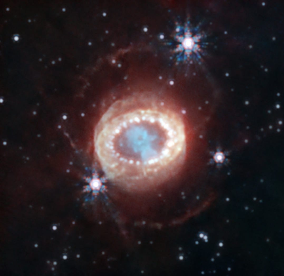 A thick and fuzzy ring of material glows eerily surrounding a blobby blue structure shaped like a keyhole. Two very faint arcs of light extend above and below it. Stars are scattered throughout. A thick and fuzzy ring of material glows eerily surrounding a blobby blue structure shaped like a keyhole. Two very faint arcs of light extend above and below it. Stars are scattered throughout.