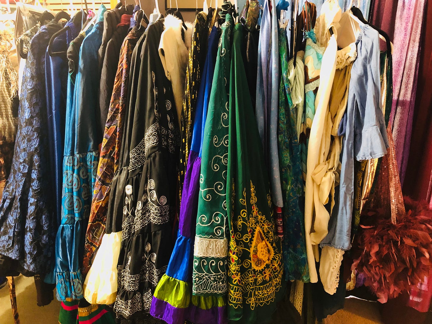 Free standing clothes rack stuffed with a rainbow of embroidered skirts, fancy shirts, and feather-laden extravaganzas.